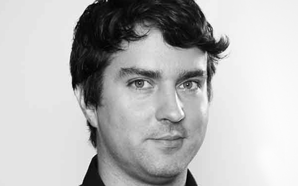 Black and white close-up portrait of a man with dark, wavy hair looking toward the camera.