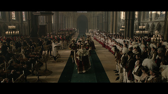 People in historical attire gathered in a large, dimly lit hall with high vaulted ceilings.