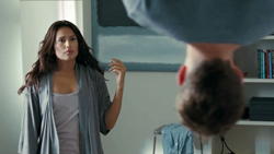A woman with long dark hair looks toward a man in the foreground who is seen from behind.