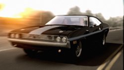 A black vintage muscle car driving along a road during a golden sunset.