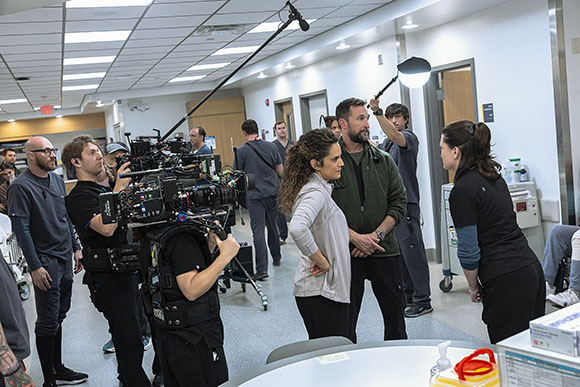 A film crew with a large camera and lighting equipment filming a scene in a bright room.