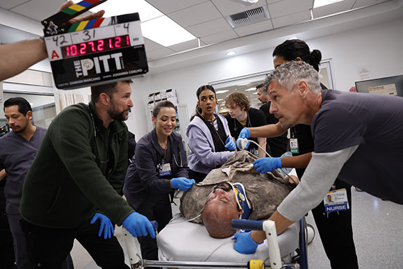 Film crew members surround an actor lying on a medical gurney during a production.