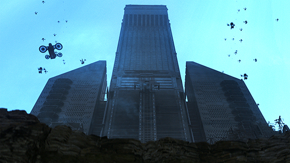 A low-angle view of a colossal, dark skyscraper flanked by two smaller structures under a blue sky.