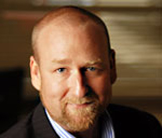 A man with light skin, a bald head, and a reddish-brown beard looking toward the camera.