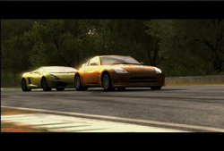 A yellow sports car follows an orange sports car on a paved racing track with trees in the background.