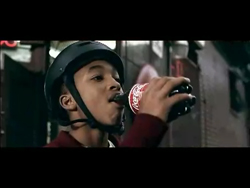 A young person in a black helmet drinks from a dark glass bottle with a red and white label.