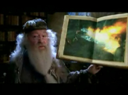 An elderly man with a long white beard and glasses holds up an open book showing an illustration of fire.
