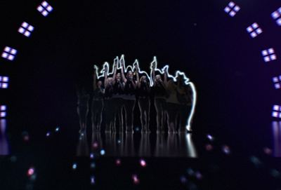 Silhouetted performers with raised hands stand on a dark stage under a bright backlight.
