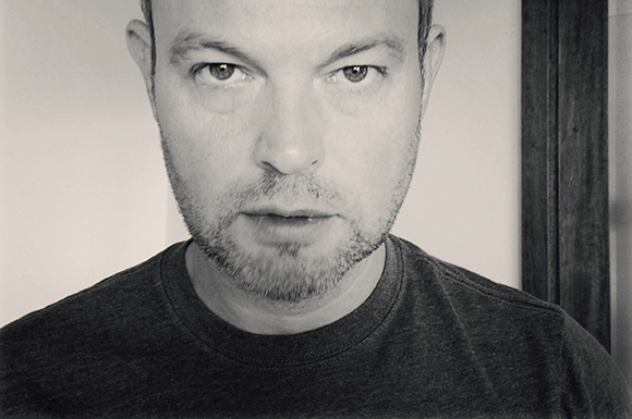 Black and white close-up portrait of a man with light facial hair looking forward.