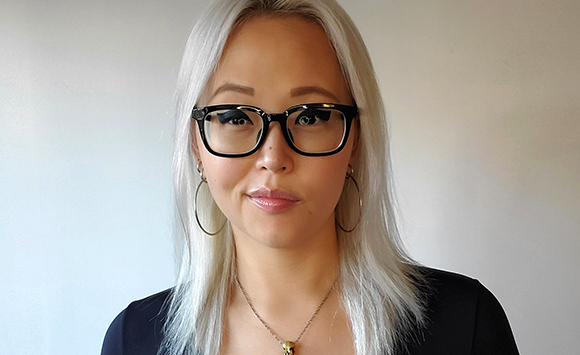 A woman with long platinum blonde hair and black-rimmed glasses looking at the camera.