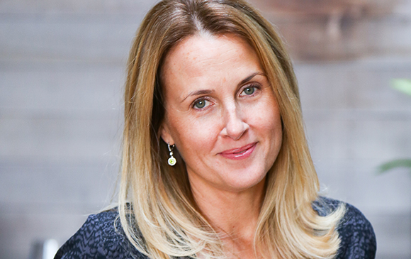A blonde woman with light eyes and a slight smile looking toward the camera.