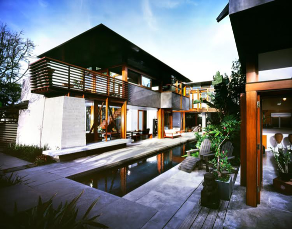 A modern two-story home with wood and concrete architecture surrounding a long, narrow reflecting pool.