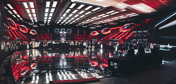 A large, dark command center with red glowing lights, multiple monitors, and a highly reflective floor.