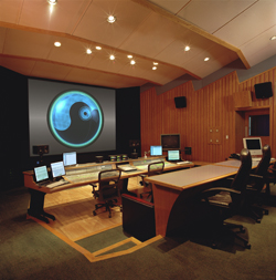 A dark presentation room featuring a large circular graphic on a screen and several computer workstations.