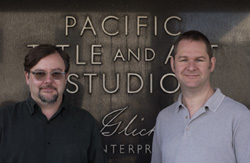 Two men smiling in front of a dark wall with the words Pacific Title and Art Studios.