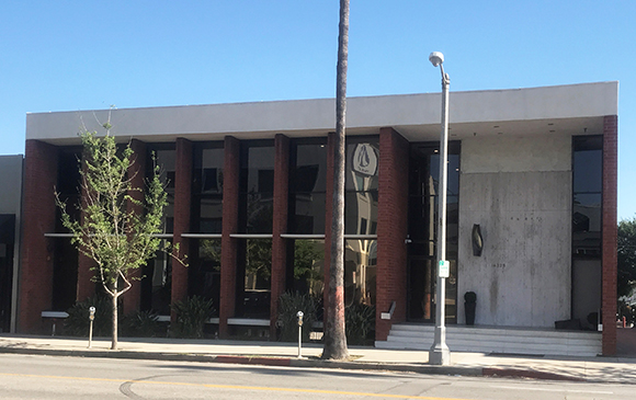 A modern two-story building with dark brick pillars, large glass windows, and a concrete facade.
