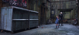 A person in a blue coat stands near a person in dark armor in a dark, industrial alleyway.
