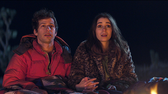 A man in a red puffer jacket and a woman in a leopard print coat sit together at night.