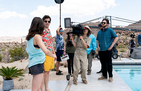 A film crew operates a large camera and lighting equipment outdoors near a swimming pool.