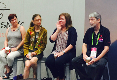 Four people, three women and one man, sit on stools in a panel discussion. The women are on the left, and the man is on the r