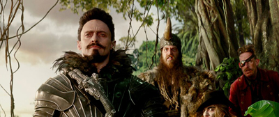 Four people in fantasy costumes stand amidst trees and vines in a forest setting.