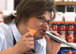 A person eating a triangular chip while holding a silver microphone to their mouth.