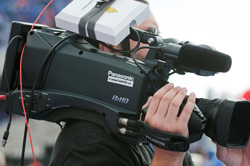 A person holding a large black Panasonic professional video camera with a microphone attached.