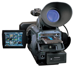 A professional black video camera with a large lens hood and an open side compartment showing a disc.