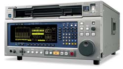 A silver electronic testing device with a blue digital screen, numerous buttons, and a large rotary dial.