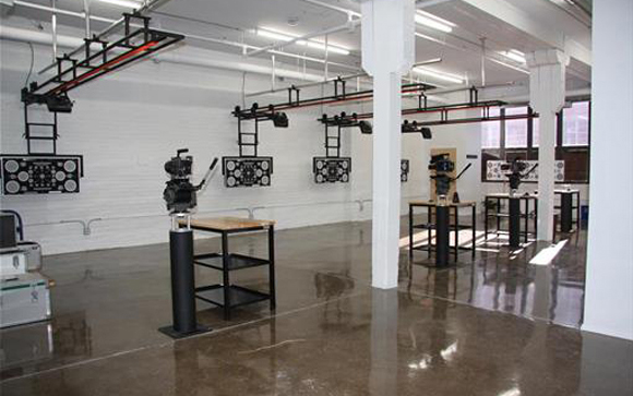 A film studio with overhead lighting rigs, cameras on pedestals, and polished concrete floors.