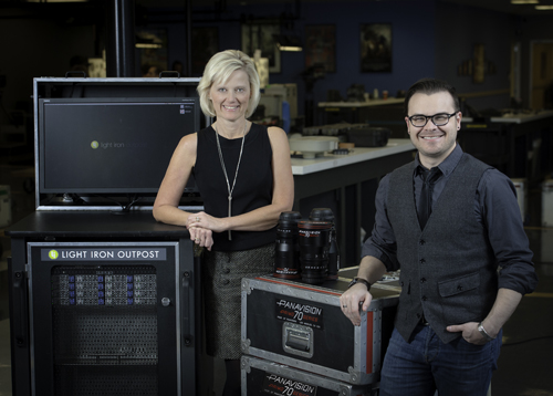 A woman in a black tank top and a man in a grey vest stand beside film equipment and monitors.