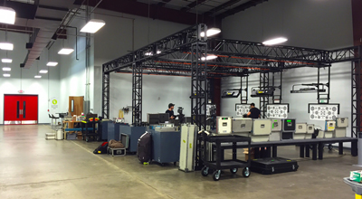 A spacious industrial warehouse containing a black metal truss frame, workstations, and various technical equipment.