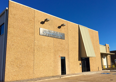 A tan, textured building with a Panavision sign and a yellow awning under a bright blue sky.