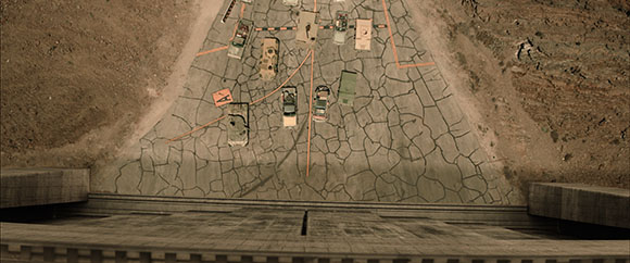 Aerial view of several vehicles driving on a heavily cracked asphalt road between two hills.