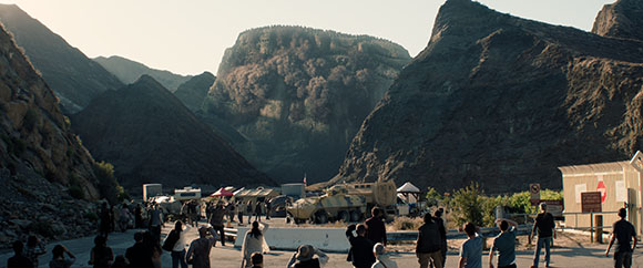 A crowd of people standing in a wide valley surrounded by large, rugged mountains under a clear sky.