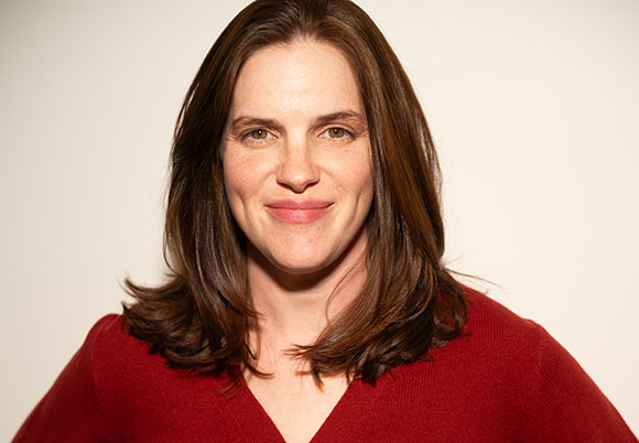 A woman with shoulder-length brown hair and a slight smile, wearing a red V-neck sweater against a plain background.