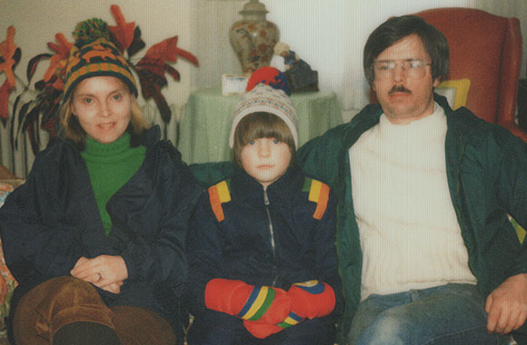 A man, woman, and child sit together indoors wearing winter clothing.