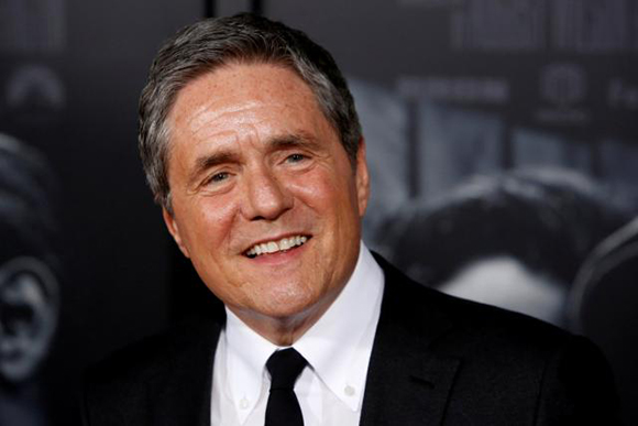 A smiling middle-aged man with graying hair wearing a black suit, white shirt, and black tie.