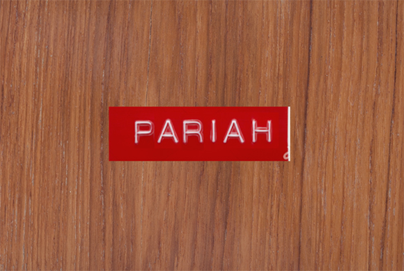 The word PARIAH in white capital letters on a red rectangular label against a brown wood background.