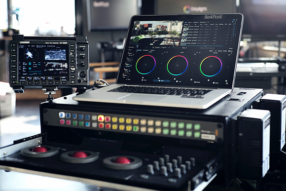 A laptop displaying color wheels sits atop a professional video editing console and hardware rack.