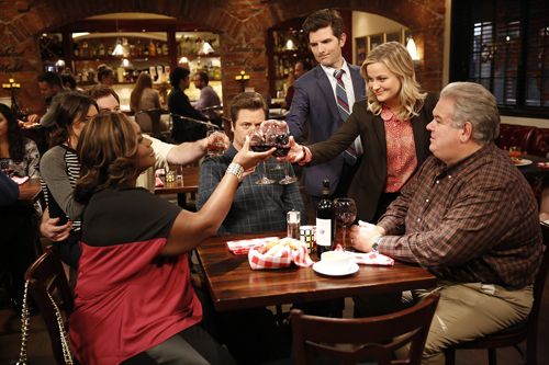 A group of people sitting around a wooden table in a restaurant, raising wine glasses for a toast.