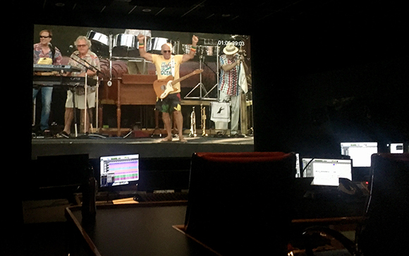 A large screen displays a band performing on stage with a drummer, keyboardist, guitarist, and singer.