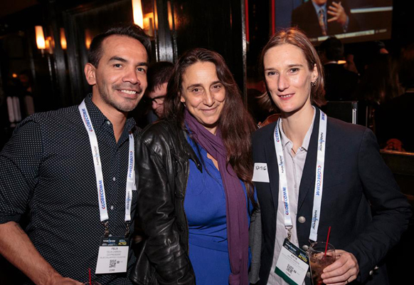 A man and two women wearing lanyards pose together at an indoor evening event.