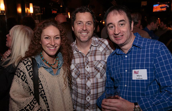 A woman with curly hair and two men smiling together at an indoor social event.