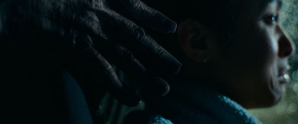 A dark, wrinkled hand is placed gently on the side of a person's head, obscuring part of their face.