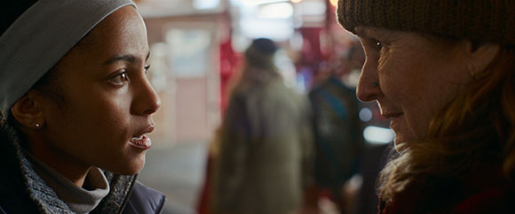Two women in profile, one with a grey headband and the other wearing a knit cap, appear to be in conversation.
