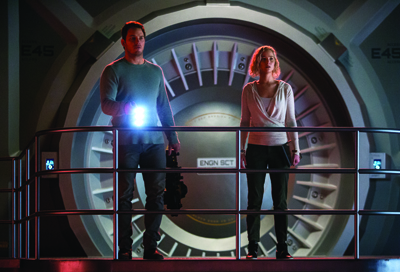 A man and woman stand on a platform in front of a large, circular, metallic sci-fi door.