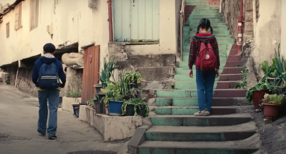 A person in a red plaid shirt walks up green-painted stone stairs in a narrow alley.