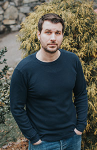 A man with short brown hair and a beard wearing a dark blue long-sleeved shirt.