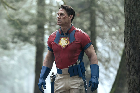 A man in a red and blue superhero suit with a yellow emblem stands in a misty forest.